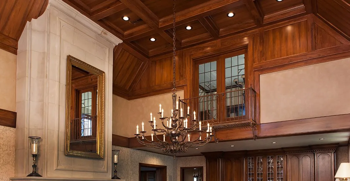 Grand room with wood-paneled coffered ceiling, balcony and candle chandelier